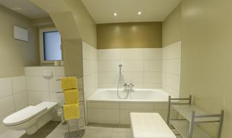 A modern bathroom with a bathtub and a toilet. The walls are light and the space is well-lit.