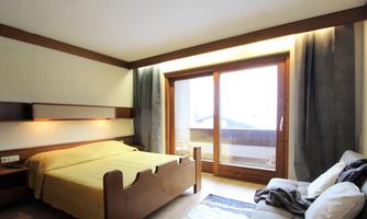 A cozy bedroom with a large window and a beautiful view. The decor consists of wood and a yellow bed sheet.