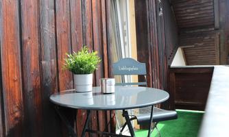 A small balcony with a round table and a chair. On the table, there is a flower pot and a candle.