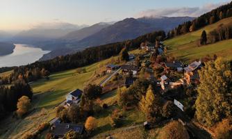 A picturesque landscape with a small village in the mountains. The sunset is reflected in the nearby lake, and the colorful autumn trees add warmth to the scene.