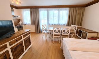 A bright and modern room with wooden flooring. There is a dining table, chairs, and a television.