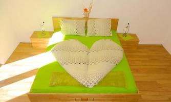 A bed with a heart-shaped arrangement of pillows and bedding in vibrant green. The room is bright and minimalist in design.