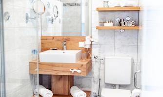 A modern bathroom with wooden shelves and an elegant sink. Clean towels are ready, and the decor is bright and inviting.