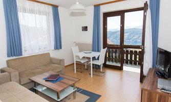A cozy living room with a couch, table, and chairs. Large windows offer a view of the mountains.