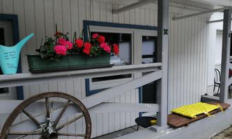 A cozy porch with colorful flowers in a box and an old wagon wheel. Next to the porch lies a yellow blanket on a wooden board.