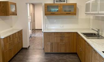 A modern kitchen with wooden cabinets and light walls. The countertop is made of white marble and the kitchen has ample space for cooking.