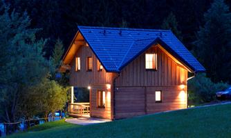 A charming wooden house, illuminated at night. Surrounded by trees, it exudes a cozy atmosphere.