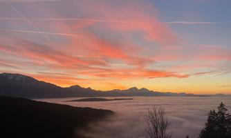A breathtaking sunrise over a sea of fog. The mountains in the background are faintly visible, and the sky is tinted in warm colors.