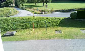 A green lawn with a playground and a gate for children. In the background, there are trees and a quiet street.