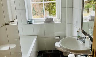 A modern bathroom with a bathtub, a sink, and a window. The walls are brightly tiled and the floor has a dark pattern.