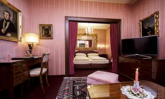An elegant room with pink walls, an antique desk, and a comfortable bed in the background. Cozy lighting creates an inviting atmosphere.