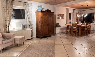 A cozy living space with a bright, inviting dining area. On the left side, there is a pink armchair and a wooden cabinet.