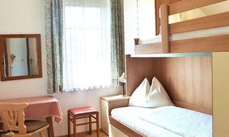 A simple room with a bunk bed and a single bed. There is a table, chairs, and a window with curtains.