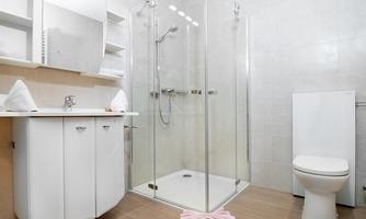 A modern bathroom with a glass shower and a white toilet. The walls are light, and the floor has a neutral color scheme.