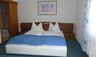 A friendly bedroom with a large double bed and two pillows. The walls are light and there is a nice hue in the room.