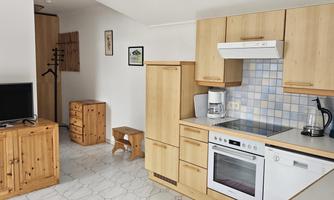 A modern kitchen with wooden cabinets and appliances. In the background, there is a television and a seating area.