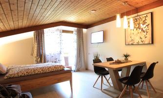A cozy room with a double bed and a dining table. Large windows provide plenty of daylight.