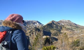 A hiker looks at an impressive mountain landscape with snow-capped peaks. The sky is clear and blue.