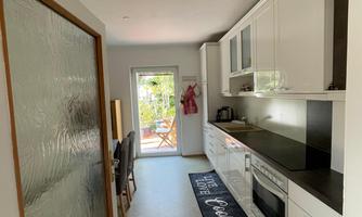 A modern kitchen with white cabinets and a charcoal-colored countertop as well as dining table. Direct access to the terrace and garden.