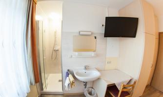 A simple guest room with a sink, a TV, and a table. There is also a shower in a separate corner of the room.