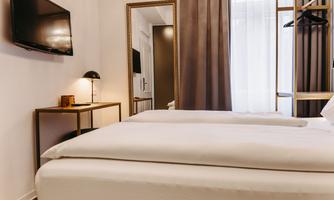 A modern bedroom with a large bed and a television on the wall. The room has large windows and stylish furniture.