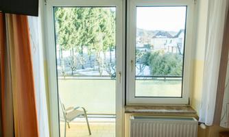 A window overlooking a balcony and a garden. Outside, trees and some houses are visible.