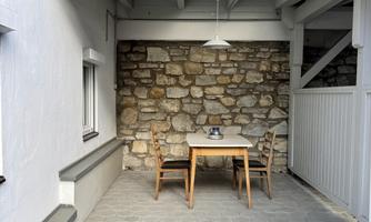 An inviting courtyard with a table and chairs. The walls are partly clad in natural stone, and the floor is paved.