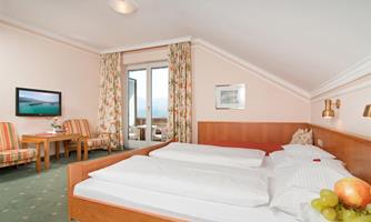 An inviting room with a double bed, a television, and a cozy seating area. Large windows offer a view of the surroundings and plenty of daylight.
