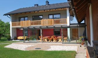 A modern house with a balcony and a spacious glass facade. The garden is designed to be low maintenance with lawn and a small gravel area.