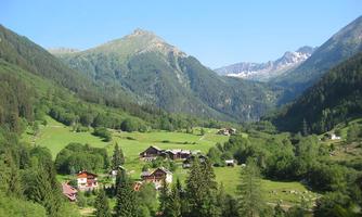 A picturesque mountain landscape with green meadows and scattered wooden houses. The majestic mountains in the background complete the idyllic scene.