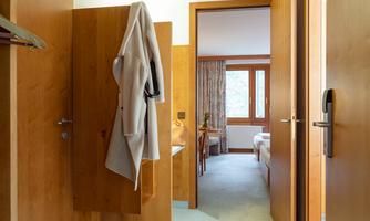 A bright hallway with wooden doors and a hook for a bathrobe. In the background, a cozy room with a window can be seen.