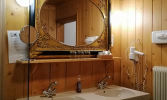 A bathroom with wooden paneling and a large decorative mirror. There are two sinks and a hairdryer on the wall.