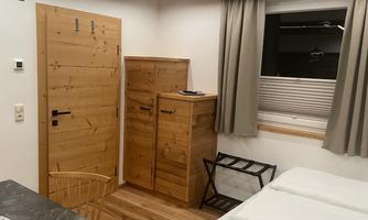 A cozy room with wooden furniture and a large window. The walls are light, and the decor feels modern and inviting.