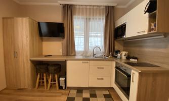 A modern kitchen with wooden paneling, a countertop, and a stove. A curtain hangs in front of the window, and there are bar stools next to the kitchen counter.
