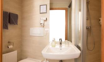 A modern bathroom with a shower and a sink. The walls are light and the furnishings are stylish and functional.