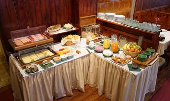 A rich breakfast buffet with various types of cheese, cold cuts, and fresh fruits. Beverages such as juices and water are also available on the tables.