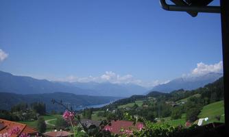 A beautiful view of green hills and mountains under a clear blue sky. In the foreground, colorful flowers are blooming.