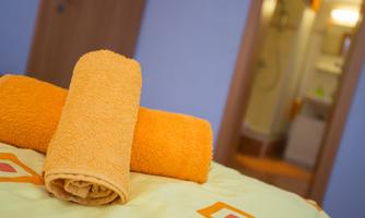 A bed with yellow towels and a colorful bed sheet. In the background, a bathroom can be seen.