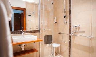 A modern bathroom with a walk-in shower and a sink on a wooden shelf. The walls are bright, and the fixtures appear functional and elegant.