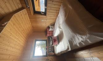 A cozy bedroom with wooden walls and a large bed. The windows offer a view of nature.