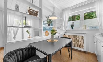 A bright dining area with a black table and a cozy chair. Large windows let in plenty of light and create an inviting atmosphere.
