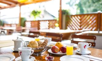 An inviting breakfast with fresh rolls, fruit, and beverages. The table is set on a cozy terrace.