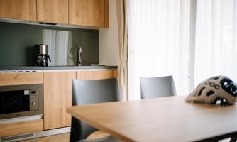 A modern kitchen with wooden cabinets and a bright atmosphere. On a table sits a bicycle helmet, next to a microwave and a coffee maker.