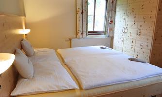 A cozy bedroom with a double bed and light wooden furniture. Soft light enters the room through the window.