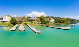 A picturesque lake with several piers and calm, green water. In the background, some buildings and trees are visible.