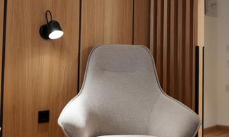A modern room with a cozy armchair and a matching ottoman. The walls are made of wood and the lighting is subtle.