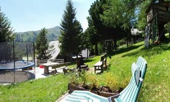 A beautiful garden with a trampoline, deck chairs, and playground equipment. Surrounded by tall trees and a picturesque landscape.