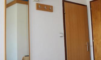 A simple room with a television on the wall. The room has a mirror, a door, and a bed with bedding.