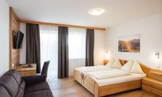 A modern bedroom with two single beds and a comfortable sofa.  
Large windows provide bright light and a cozy atmosphere.