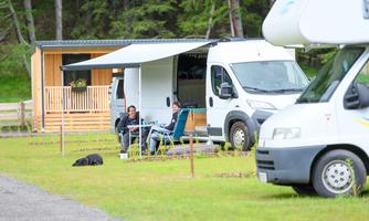 A motorhome campsite in nature. Two people relax in chairs next to their motorhome.